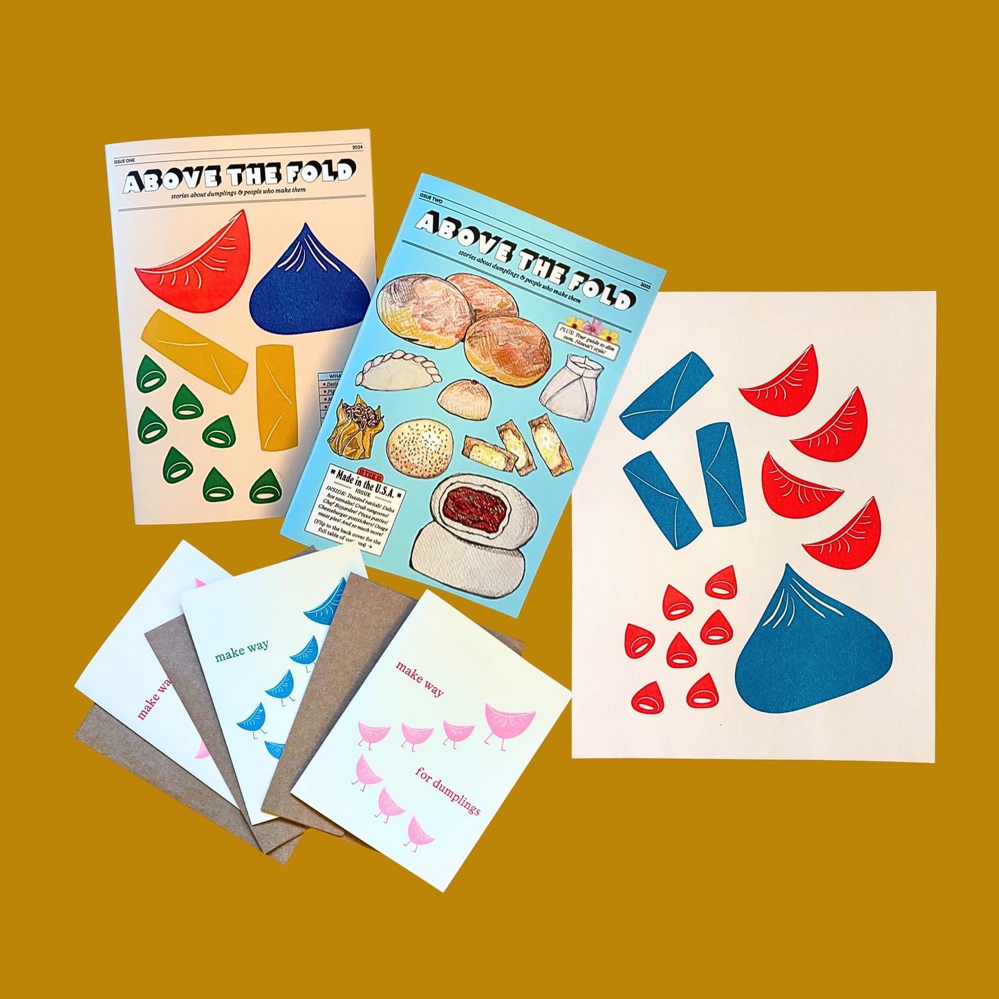 Issue 1 and Issue 2 of the Above the Fold zine with three notecards and the light teal and red print